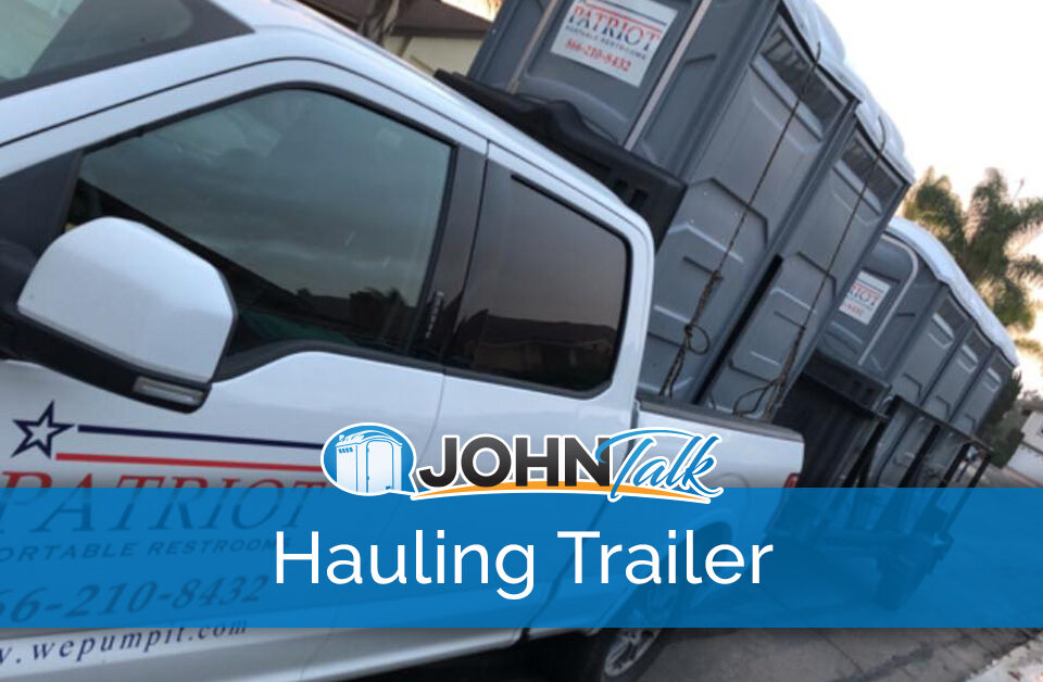 A closeup of a pickup pulling a hauling trailer with gray portable toilets
